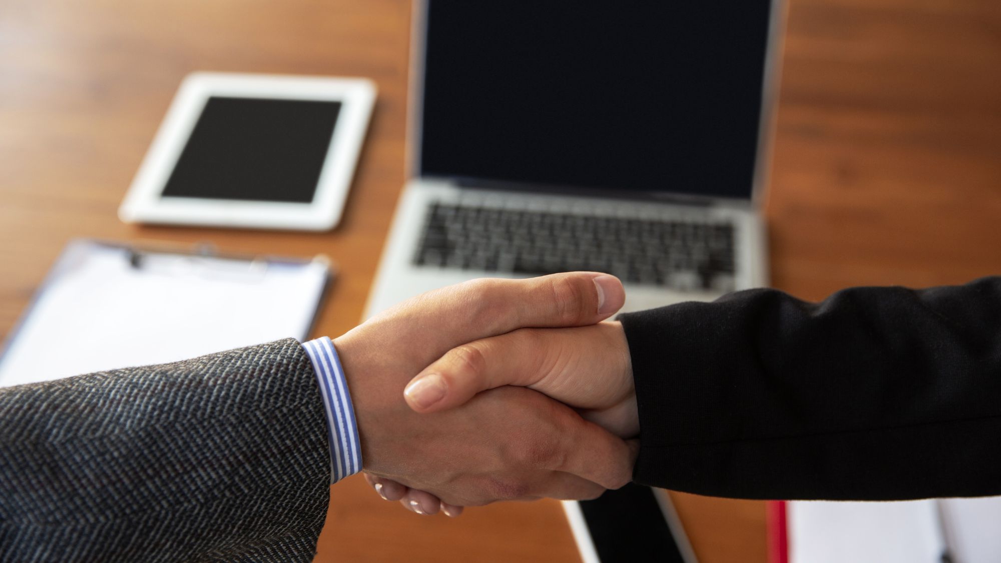 Two business professionals shaking hands over a table, symbolizing a successful partnership. Microsoft CRM 365 logo visible in the background.