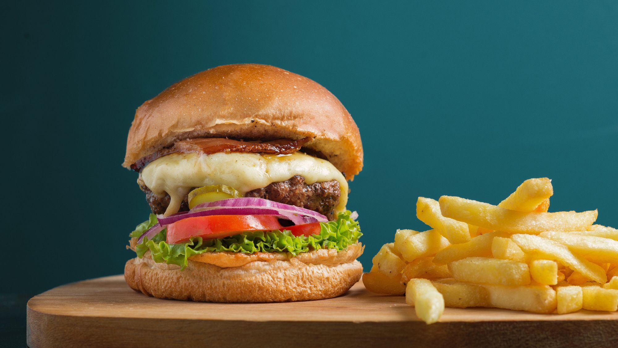 A photo of a hamburger and french fries on a wooden cutting board, representing unhealthy effects of daily fast food consumption.